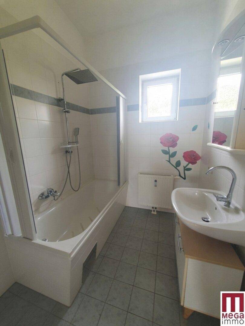 Badezimmer mit Badewanne, Dusche, Waschbecken und Fenster, dekoriert mit Rosenmotiven.