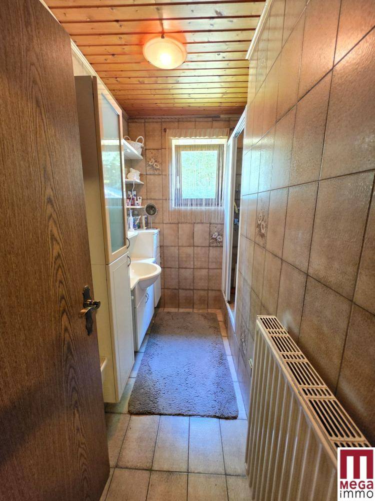 Schlichtes Badezimmer mit Dusche, Waschbecken und Fenster, gefliest in neutralen Tönen.