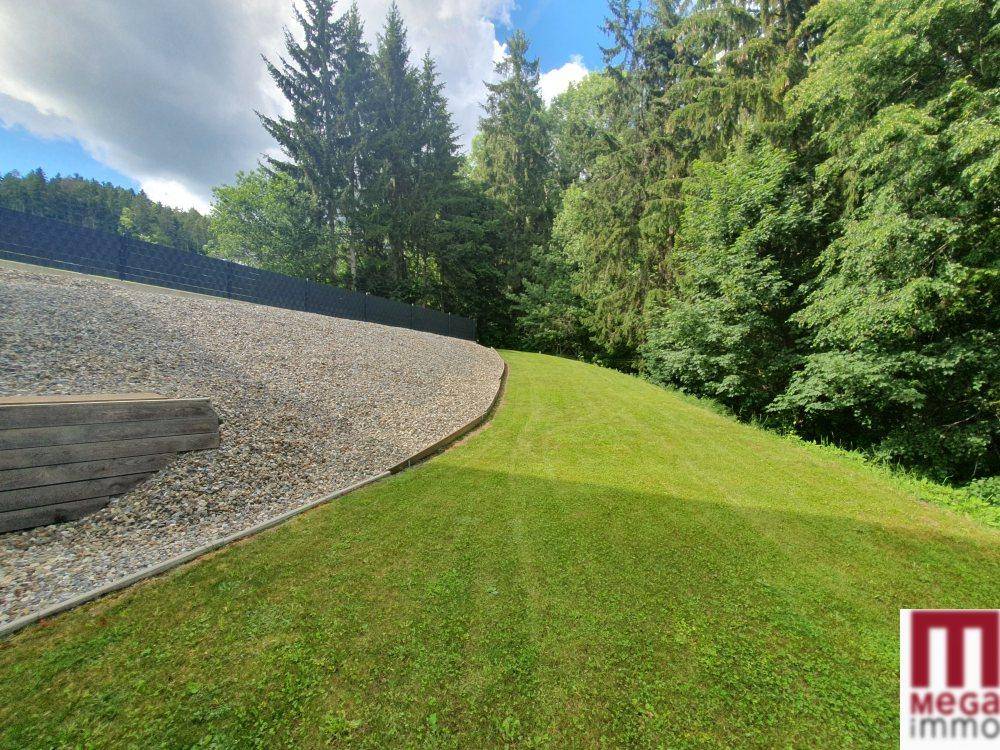 Weitläufiger Rasenbereich mit Kiesweg und dichtem Baumbestand im Hintergrund.