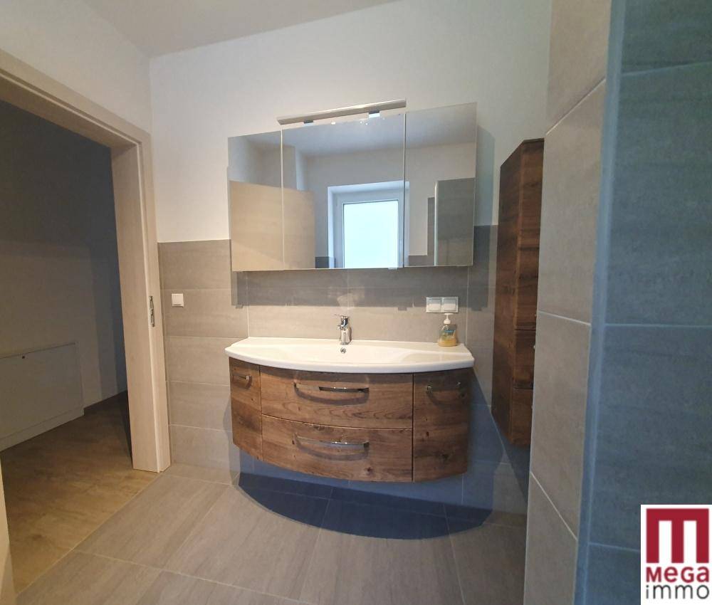 Modernes Badezimmer mit Holzwaschtisch, Spiegelschrank und grauen Fliesen, hell und funktional.