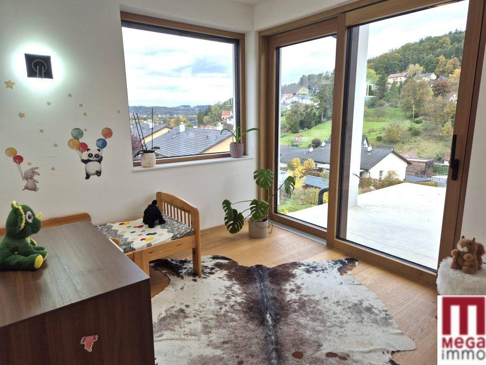 Kinderzimmer mit Holzbett, großen Fenstern und Zugang zu einem Balkon mit Weitblick.