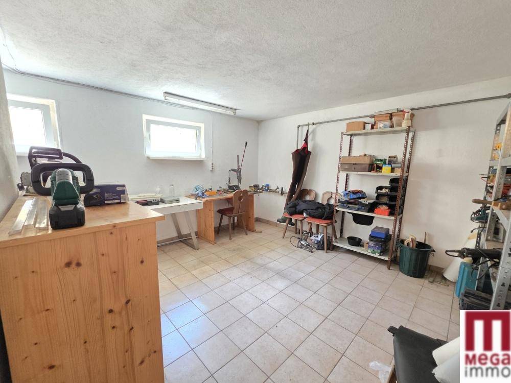 Heller Hobbyraum im Keller mit Werkbänken, Regalen und zwei Fenstern für Tageslicht.