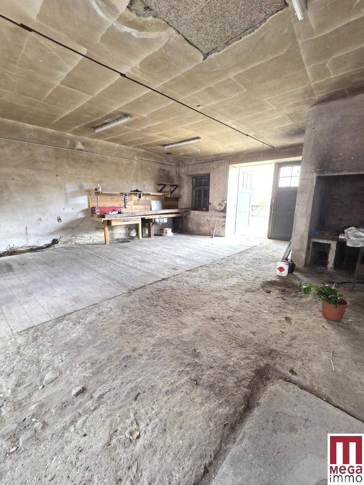 Geräumiger Werkstattbereich mit Betonboden, Arbeitstisch und einem großen Kamin oder Ofen.