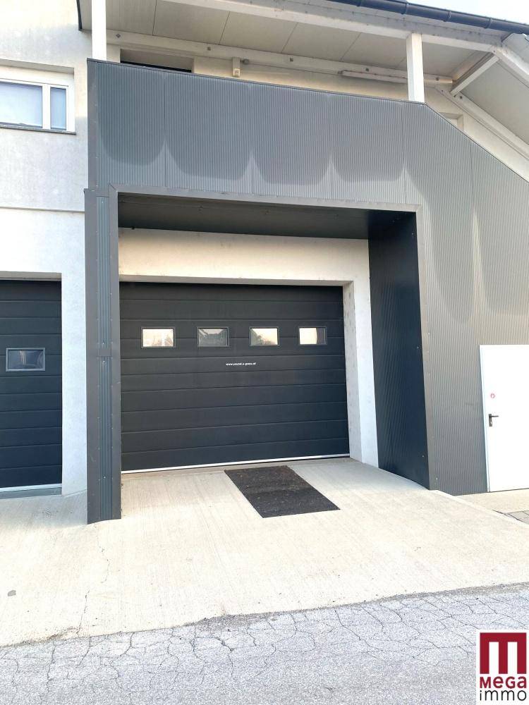 Großes, dunkles Garagentor mit kleinen Fenstern und einer Betonrampe, Teil einer modernen Gebäudefassade.