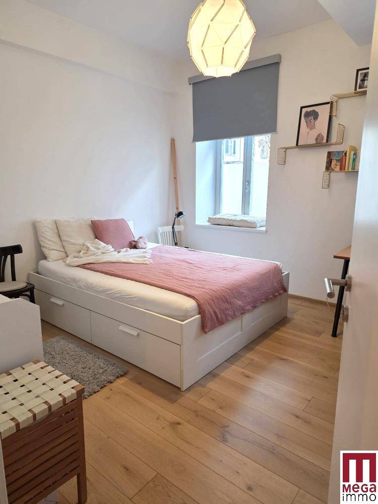 Gemütliches Schlafzimmer mit Holzboden, weißem Bett und Fenster mit Rollo.