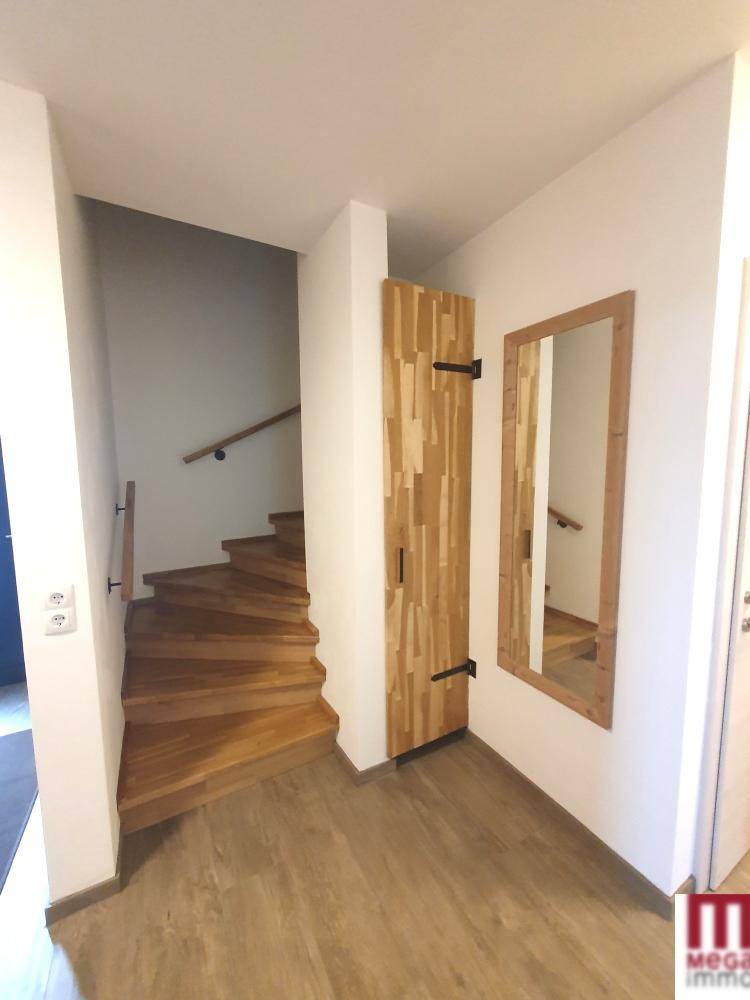 Heller Eingangsbereich mit Holztreppe und modernem Spiegel, der zu den oberen Etagen führt.