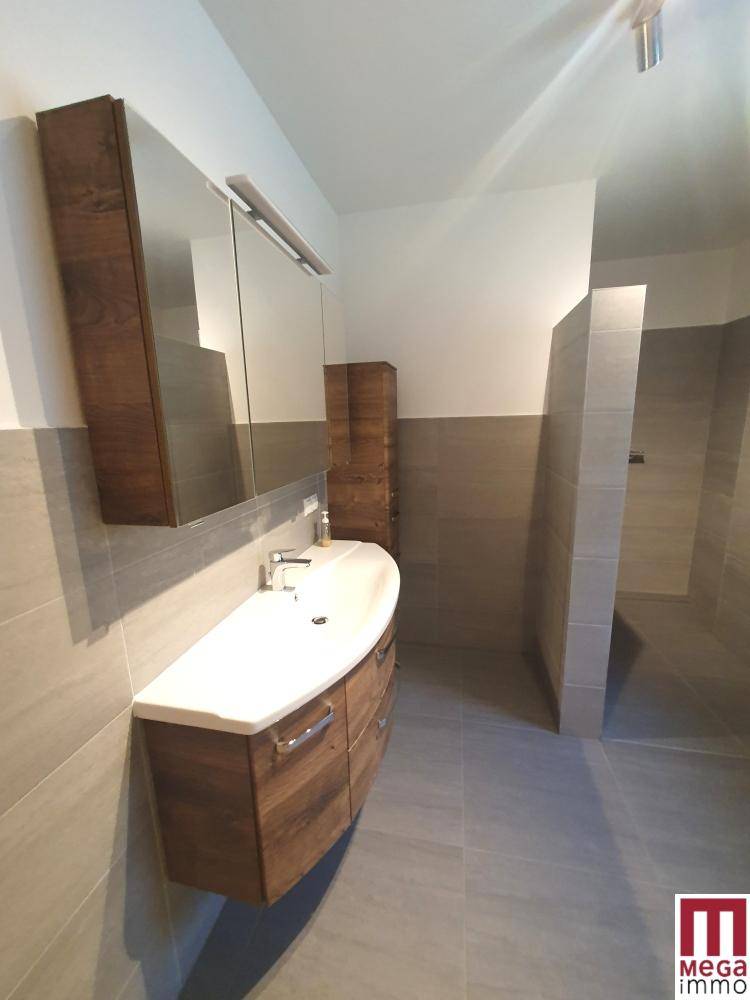 Modernes Badezimmer mit Holzwaschtisch, Spiegelschrank und begehbarer Dusche, in hellen Tönen.