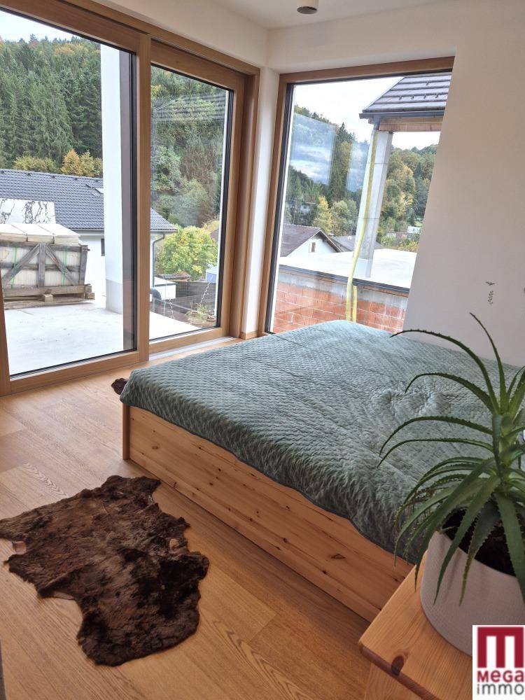 Helles Schlafzimmer mit Holzbett, großen Fenstern und Zugang zu einem Außenbereich.