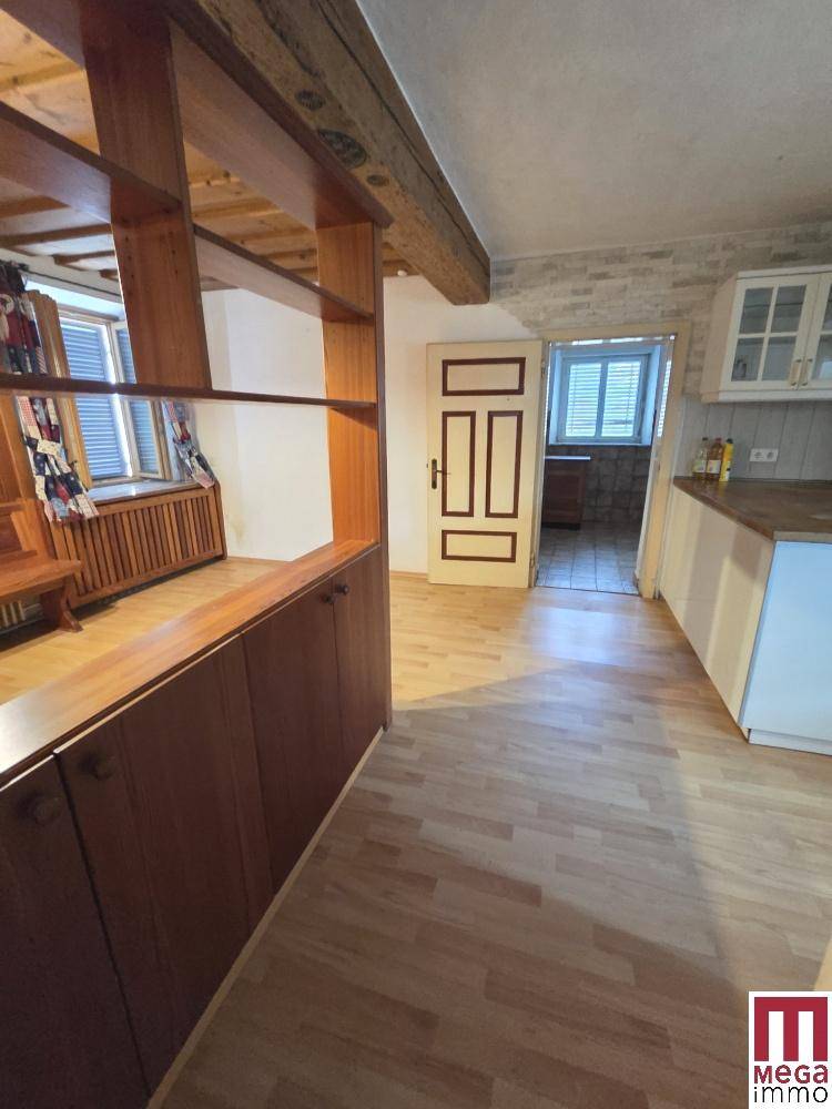 Küche mit Holzboden und offenem Übergang zu einem weiteren Raum mit Holzregal.