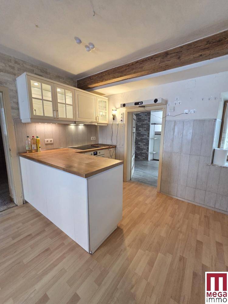 Helle Küche mit Holzarbeitsplatte, weißen Schränken und sichtbaren Holzbalken an der Decke.