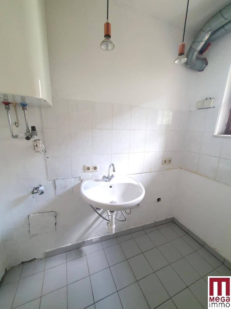 Einfacher Hauswirtschaftsraum mit Waschbecken, Boiler und gefliesten Wänden.