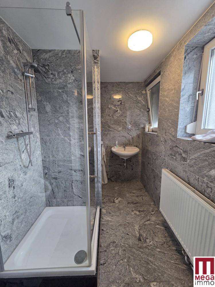 Modernes Badezimmer mit grauen Fliesen, Duschkabine und Fenster für Tageslicht.