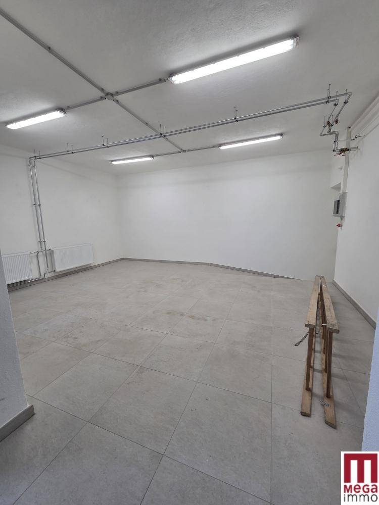 Großer, sauberer Raum mit Fliesenboden, Heizkörpern und sichtbaren Deckeninstallationen.