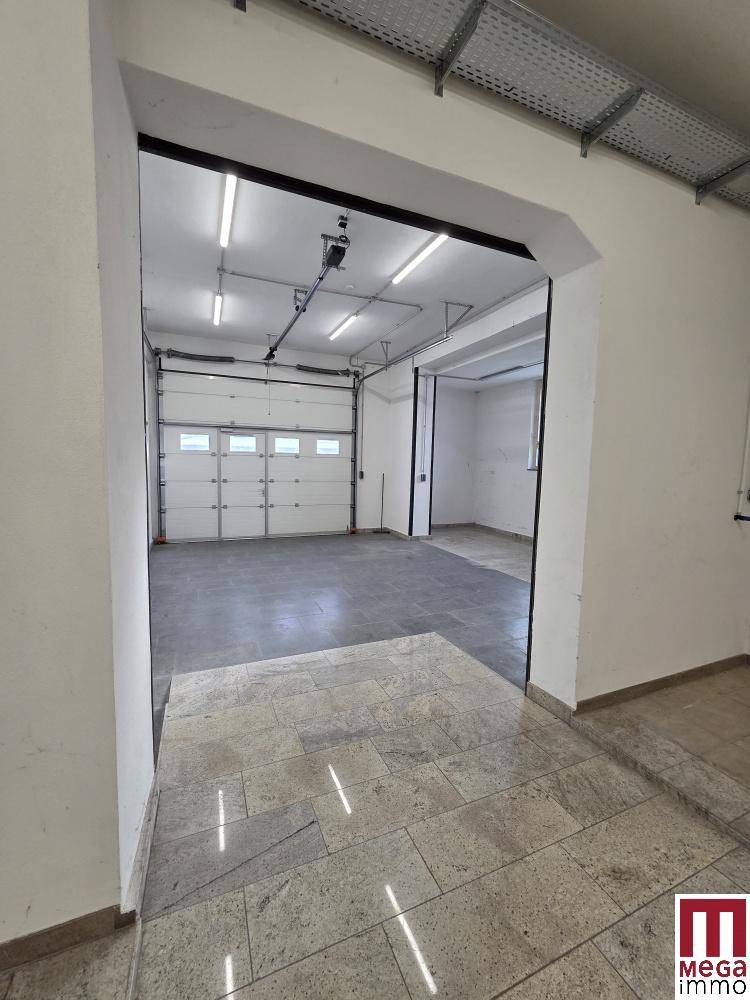 Geräumiger Innenraum mit gefliestem Boden, Rolltor und Zugang zu weiteren Bereichen.
