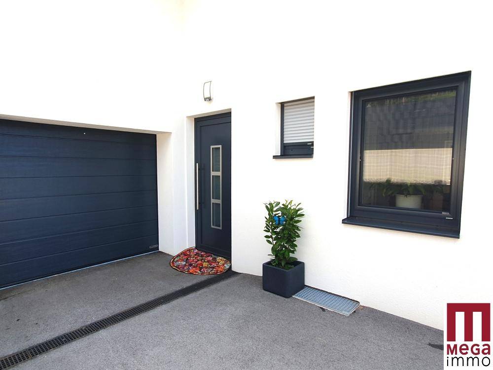 Eingangsbereich des Hauses mit moderner Haustür und integrierter Garage in dunklem Design.