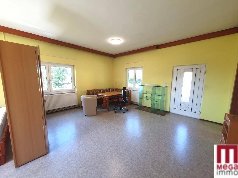 Geräumiger Wohnbereich mit gelben Wänden, Vinylboden und Holzbalken an der Decke.