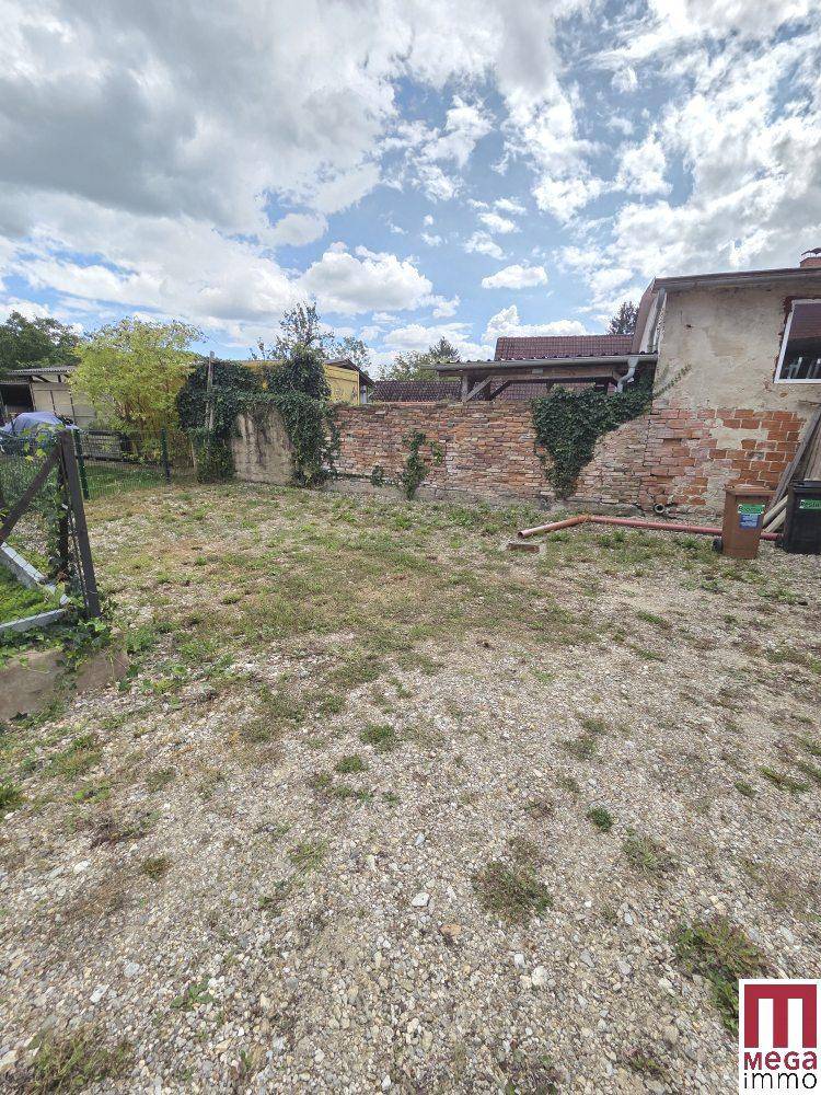 Ungepflegter Gartenbereich mit Kiesboden, alten Ziegelmauern und Bewuchs.