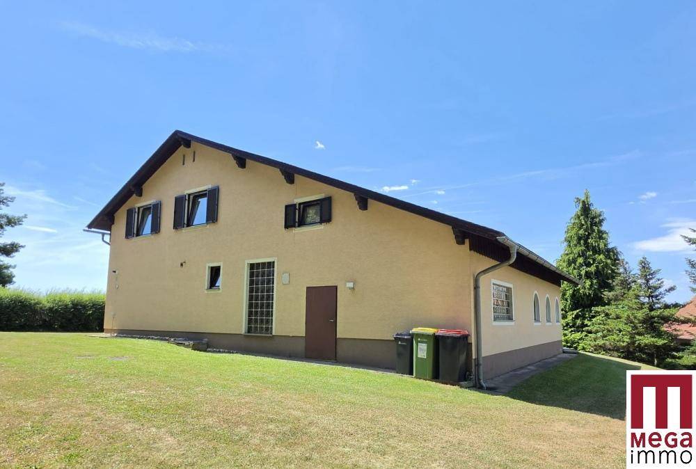 Ansicht des Hauses von der Seite mit Mülltonnen und umgebender grüner Landschaft an einem sonnigen Tag.