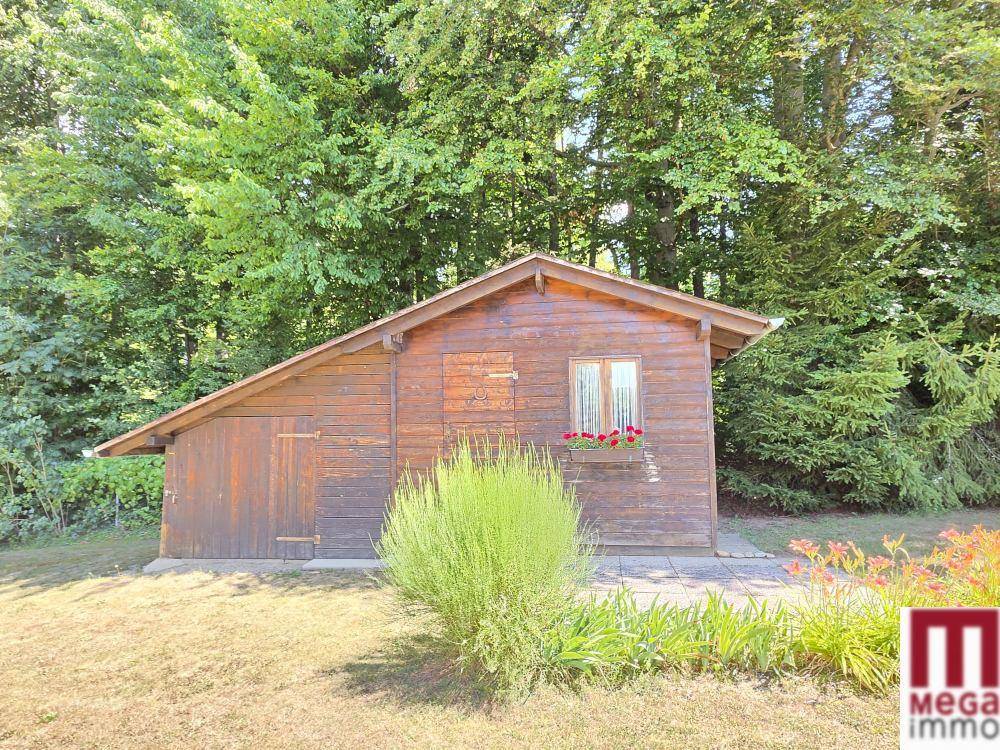 Rustikales Gartenhaus aus Holz, umgeben von Bäumen und Grünflächen.