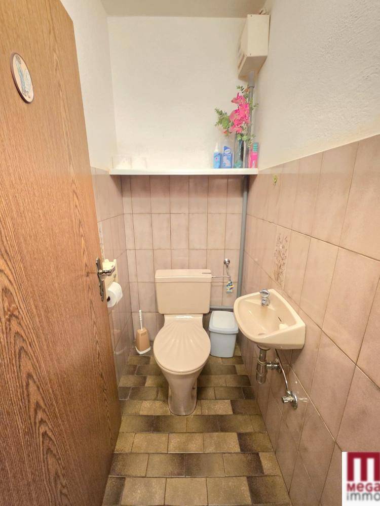 Kleines Gäste-WC mit WC und Handwaschbecken, gefliest in Pastellfarben.