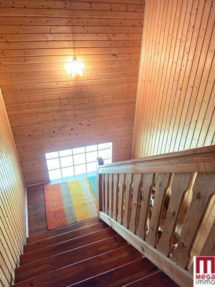 Holztreppe mit Geländer führt in das obere Stockwerk, mit Fenster für Tageslicht.