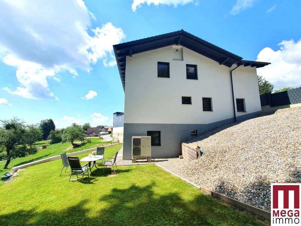 Freistehendes Einfamilienhaus mit großem Garten und Sitzbereich im Grünen unter blauem Himmel.
