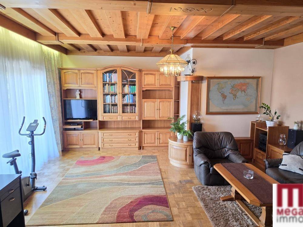 Geräumiges Wohnzimmer mit Holzbalkendecke, Parkettboden und großer Schrankwand.