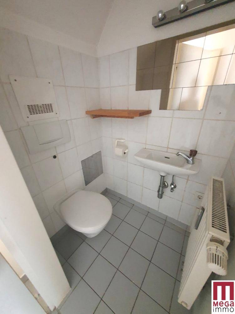 Kleiner Toilettenraum mit Fliesenboden, Wand-WC, Waschbecken und Heizkörper.