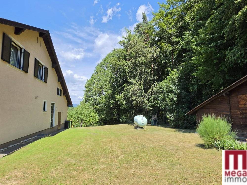 Weitläufiger Garten mit Rasenfläche, Bäumen und einem Gastank im Hintergrund des Grundstücks.
