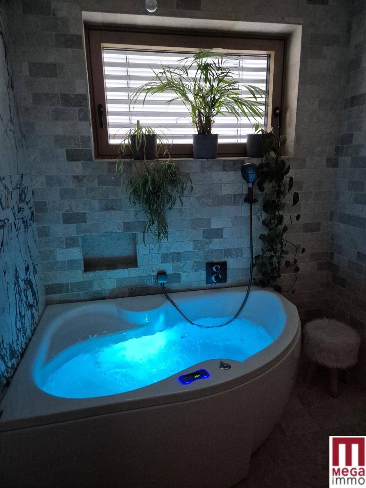Badezimmer mit Whirlpool-Badewanne, indirekter Beleuchtung und Fenster mit Pflanzen.