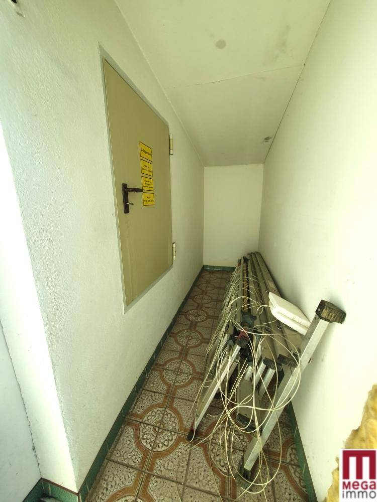Schmaler Flur mit gemusterten Fliesen und einer Tür an der Wand.