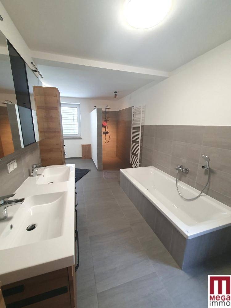 Geräumiges Badezimmer mit Badewanne, Doppelwaschbecken und begehbarer Dusche, modern gefliest.