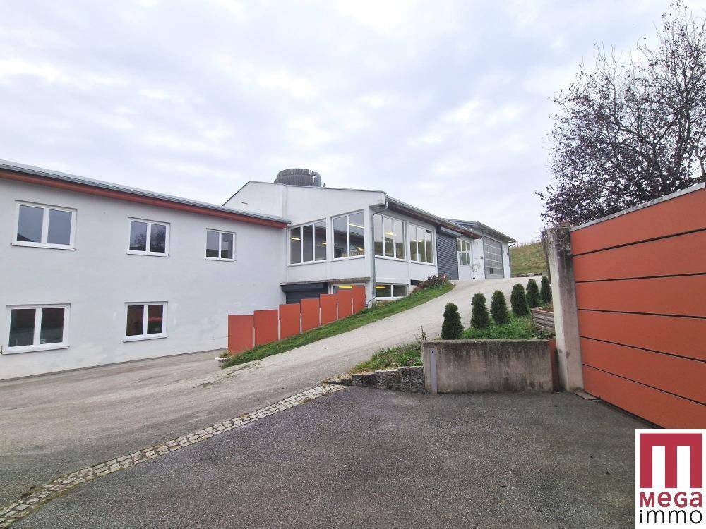 Seitenansicht des Gebäudes mit Zufahrt und weiteren Garagen im Hintergrund unter bewölktem Himmel.