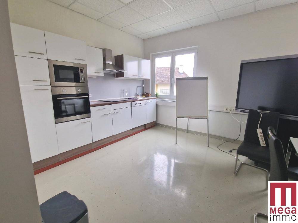 Kleine Küche mit weißen Schränken und integrierten Geräten, kombiniert mit einem Konferenzbereich.