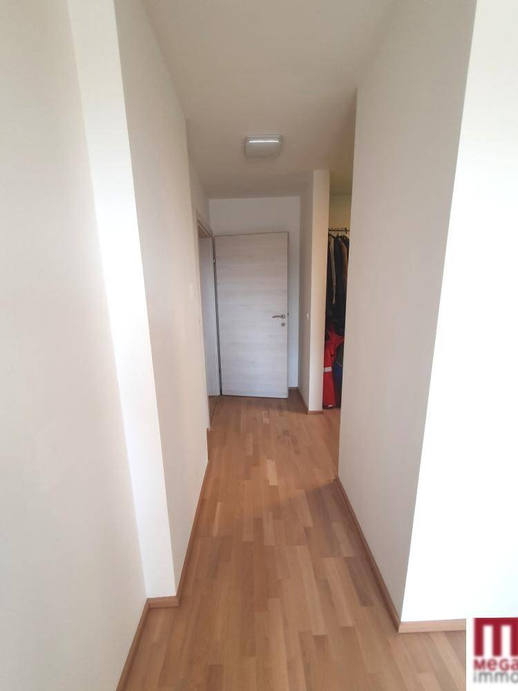 Heller Flur mit Holzboden und weiß gestrichenen Wänden, der zu weiteren Räumen führt.