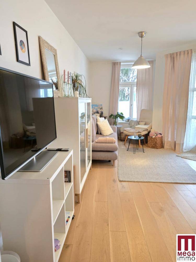 Helles Wohnzimmer mit Holzboden, beigem Sofa und großen Fenstern.