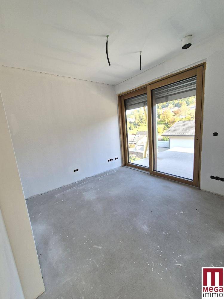 Heller, unfertiger Raum mit Betonboden und großer Schiebetür, bereit für den Ausbau.