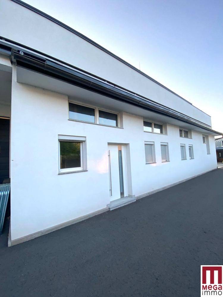 Lange, moderne weiße Gebäudefassade mit zahlreichen Fenstern und einem Haupteingang, unter klarem Himmel.