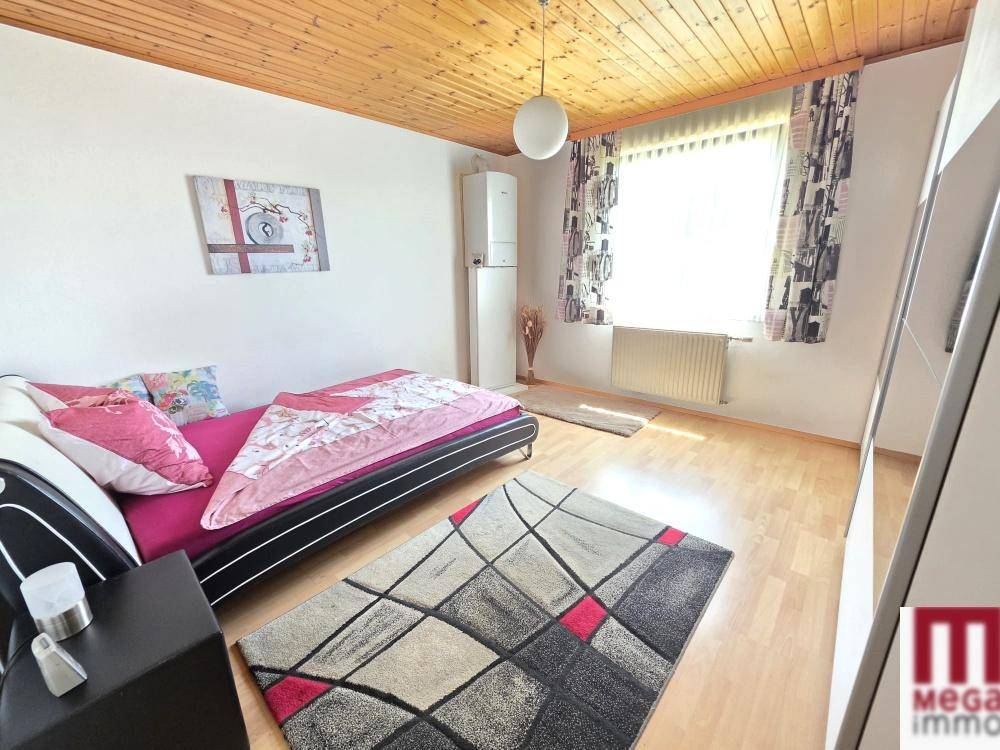 Helles Schlafzimmer mit Holzbalkendecke, Parkettboden und großem Fenster.