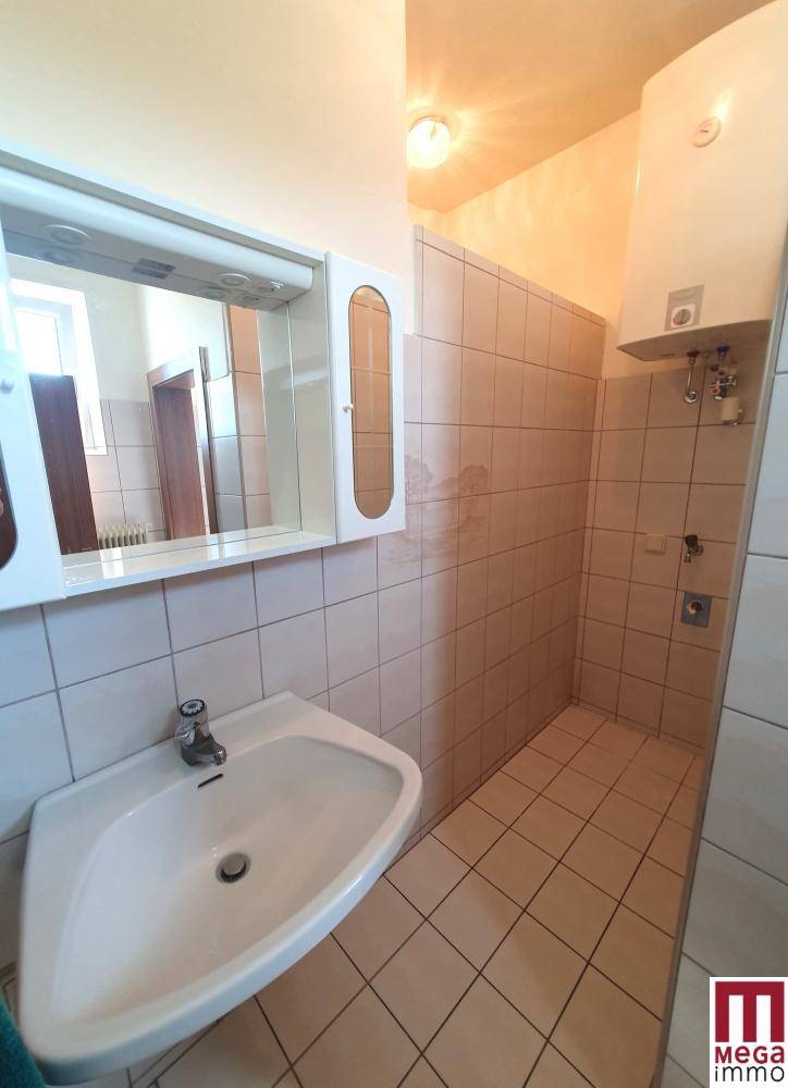 Badezimmer mit Waschbecken, Spiegelschrank und gefliesten Wänden in hellem Beige.