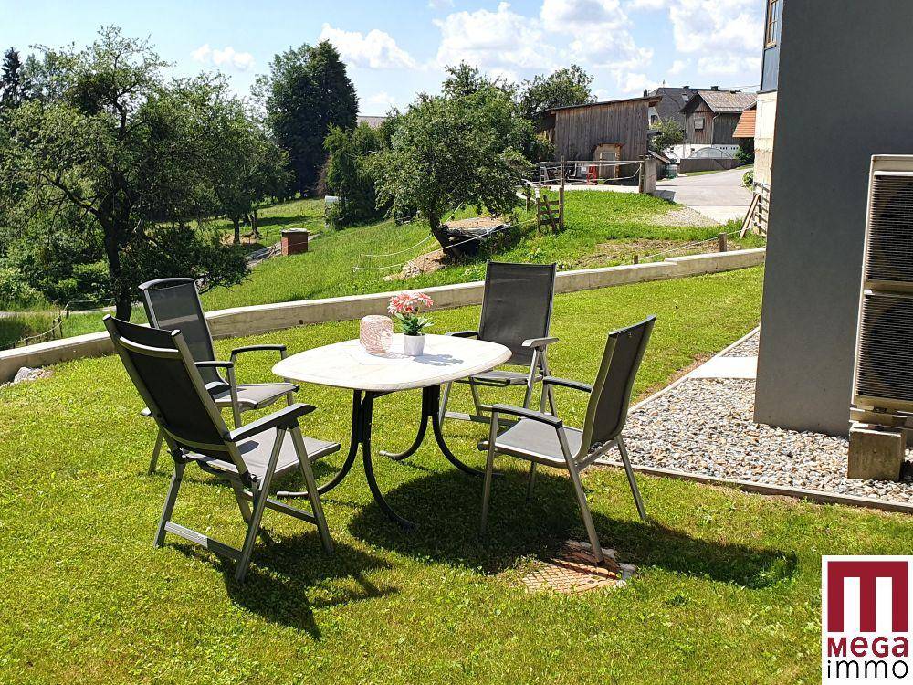 Gemütlicher Sitzbereich im Garten mit Tisch und Stühlen, umgeben von grüner Natur.