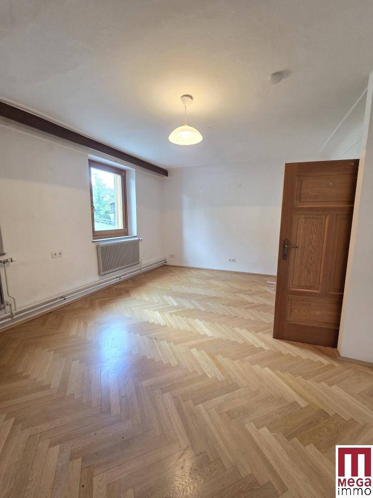 Geräumiges Zimmer mit Fischgrätparkett, weiß gestrichenen Wänden und einem Fenster.