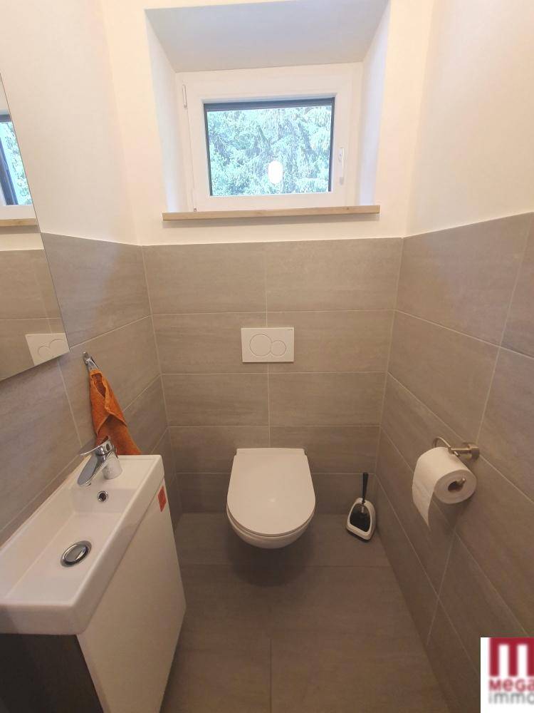 Modernes Gäste-WC mit Wand-WC, kleinem Waschbecken und Fenster, in neutralen Farben.