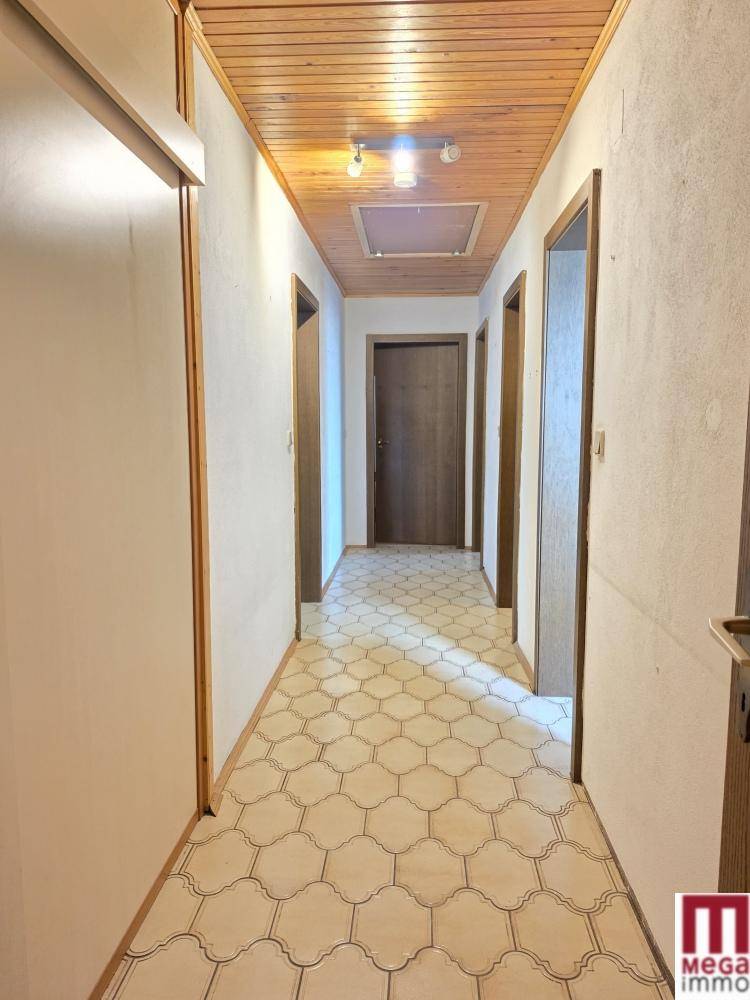 Langer Flur mit Fliesenboden und Holzdecke, der zu mehreren Zimmern führt.