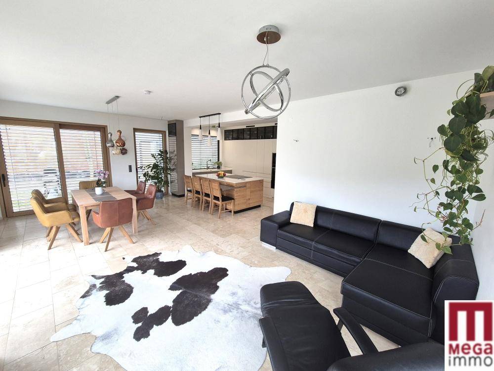 Heller Wohn- und Essbereich mit Fliesenboden, schwarzem Sofa und Blick auf die offene Küche.