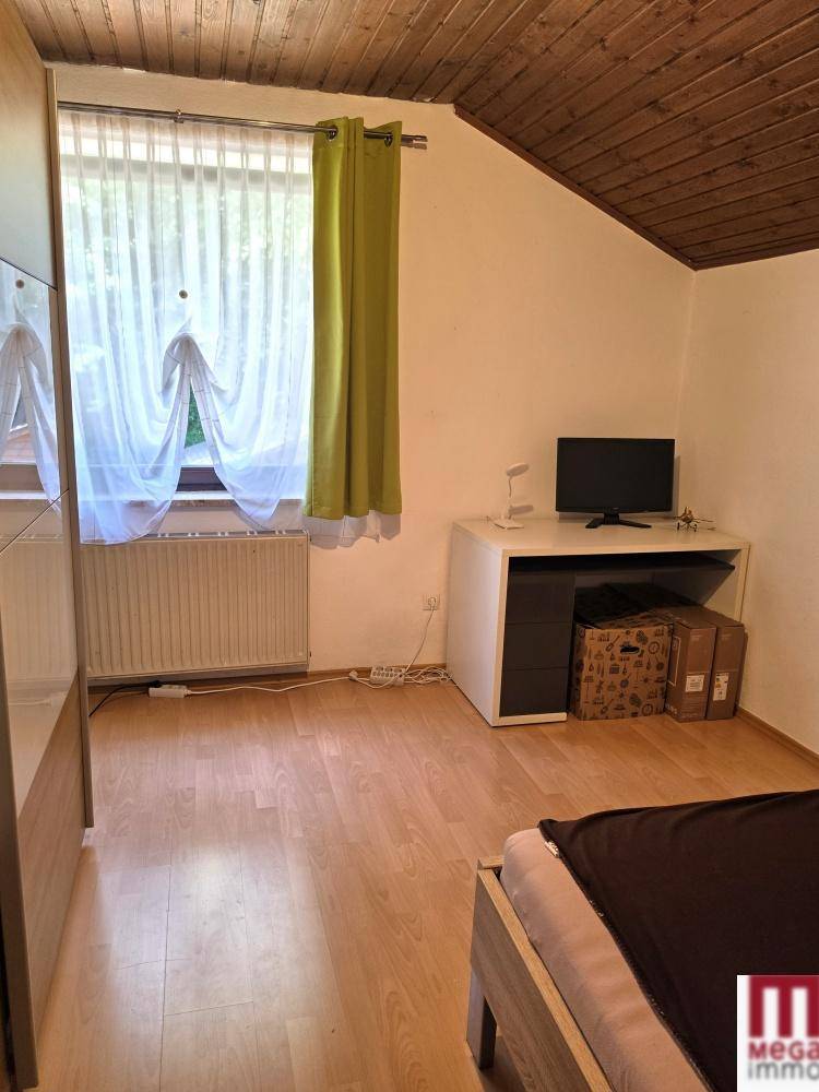 Helles Schlafzimmer mit Dachschräge, Holzbalkendecke und großem Fenster.