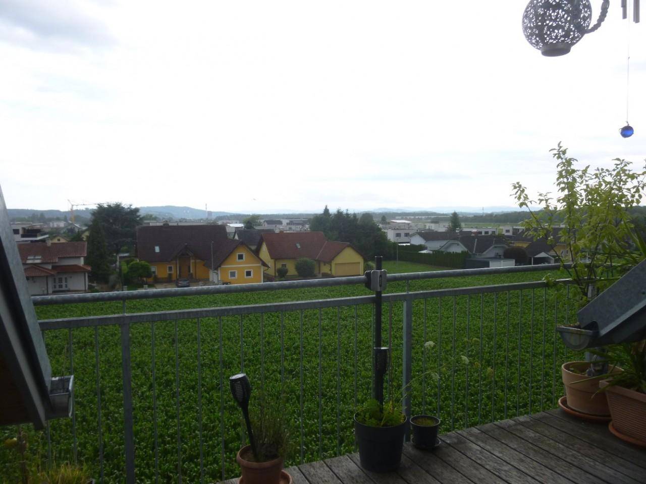 Balkon mit Holzboden, Pflanzen und weitem Blick über grüne Felder und Häuser.