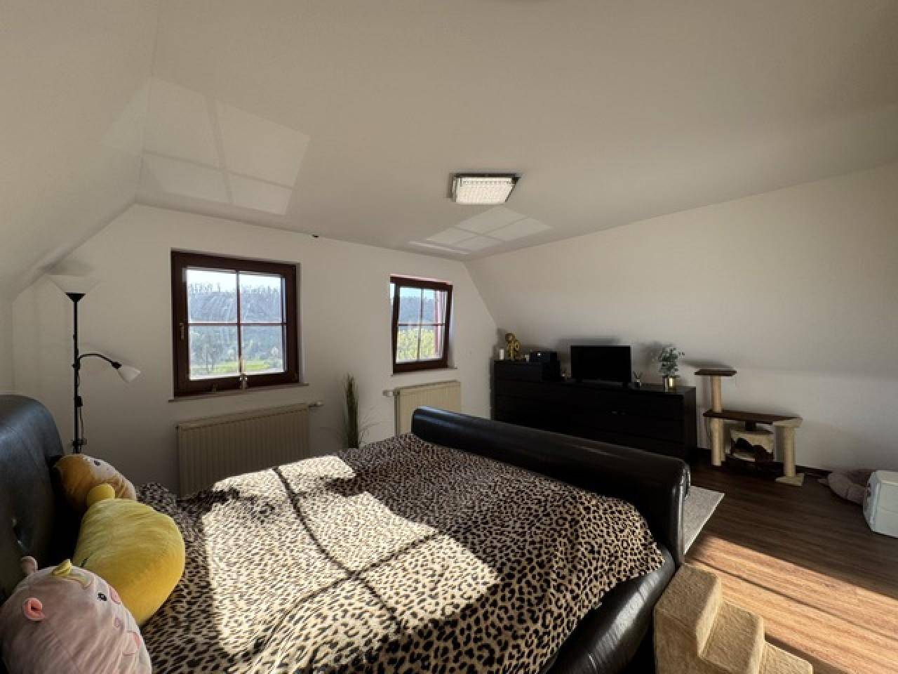 Lichtdurchflutetes Schlafzimmer mit Dachschräge, dunklem Holzboden und Blick ins Grüne.