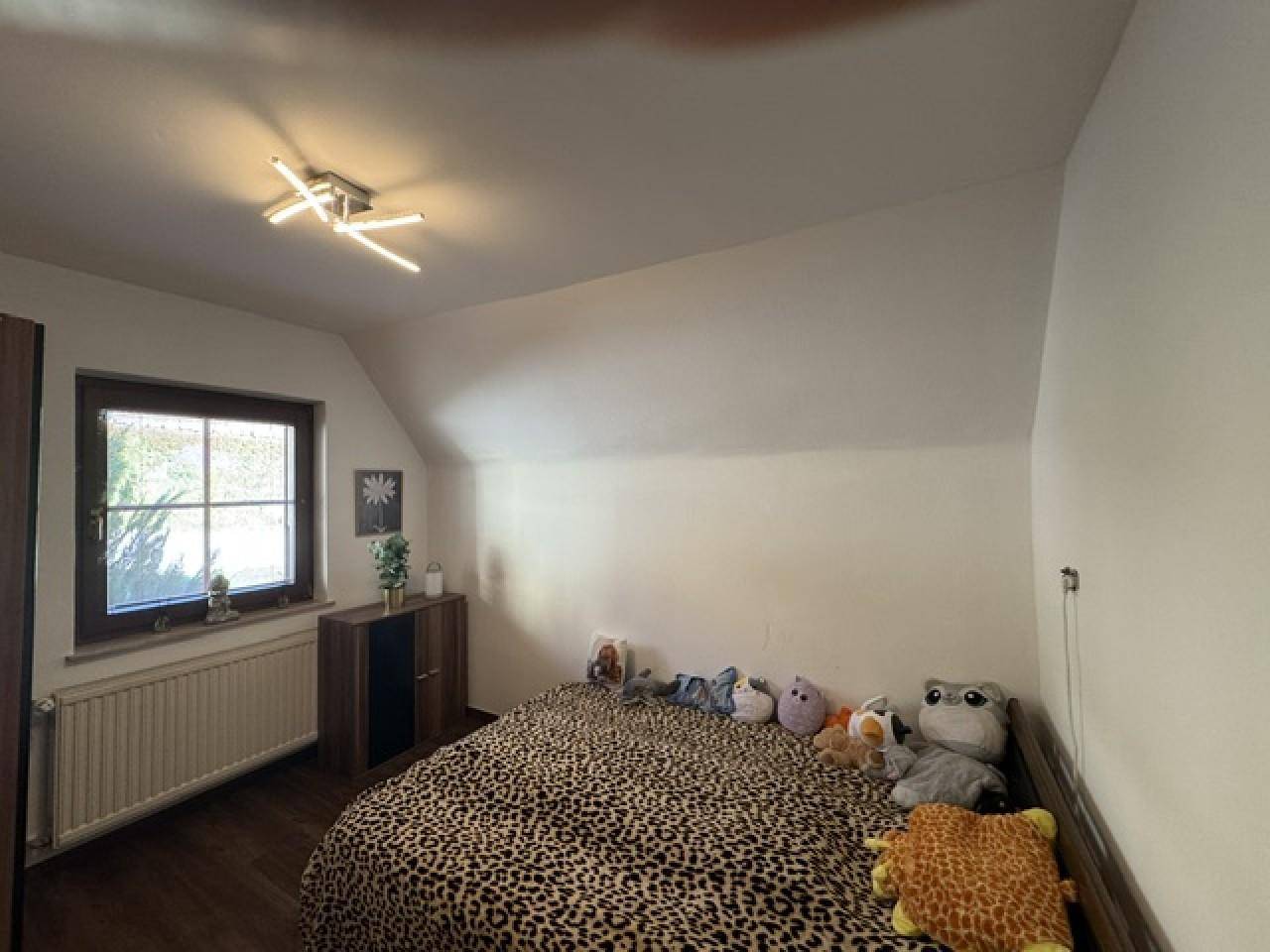 Helles Schlafzimmer mit Dachschräge, Holzboden und einem Fenster mit Blick nach draußen.