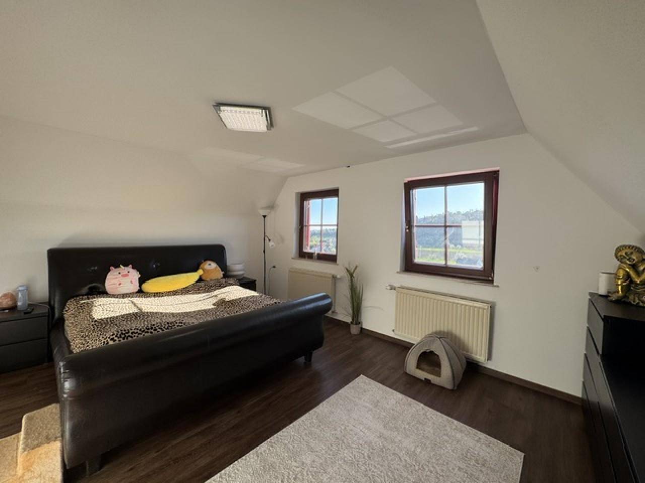 Geräumiges Schlafzimmer im Dachgeschoss mit zwei Fenstern und dunklem Holzboden.